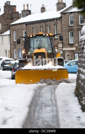 Ein Traktor mit einer Körnung Verbreitung Maschine ausgestattet Antriebe durch eine kleine verschneite Straße in Askrigg, North Yorkshire Stockfoto