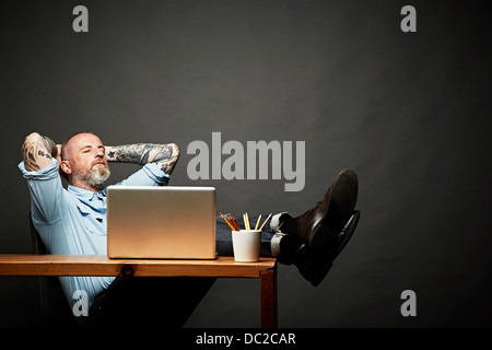 Mann, sitzend zurück mit Beine auf Tisch Stockfoto