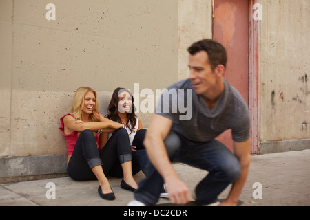 Man Eislaufen vorbei an Frauen sitzen am Boden Stockfoto