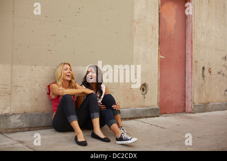 Frauen sitzen auf Boden vor Lachen Stockfoto