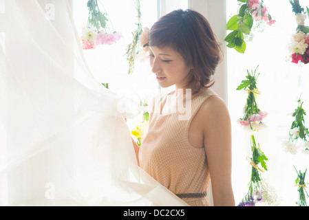 Frau, die Vorhänge der Fenster mit baumelnden Blumen heben Stockfoto