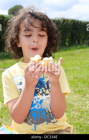 Kleiner Junge einen Donut im Park zu essen. Stockfoto