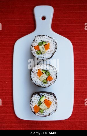 Vegetarische Maki Sushi-Rollen mit Reis, Karotten, Zucchini, grüne Bohnen, Tofu und Nori Algen in weiße Schale auf rotem Grund Stockfoto