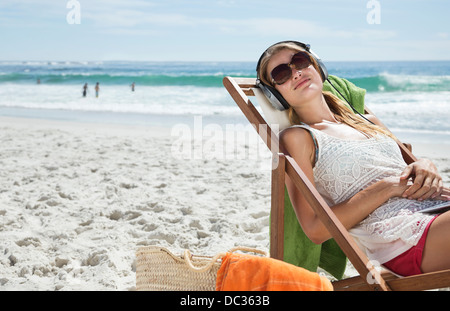 Gelassene Frau hören Kopfhörer im Liegestuhl am Strand Stockfoto