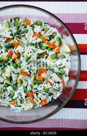 Vegetarischer Salat von weißem Reis mit gemischtem Gemüse und Tofu in eine Glasschüssel auf farbigen Hintergrund Stockfoto