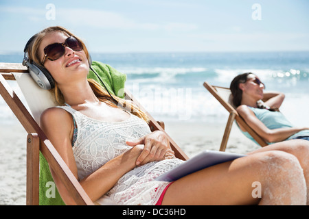 Gelassene Frau hören Kopfhörer im Liegestuhl am Strand Stockfoto