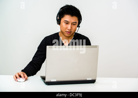 Asiatische Kunden Helpdesk Betreiber Gespräch mit einem Kunden und tragen einen Kopfhörer hinter seinem Laptop-Bildschirm Stockfoto