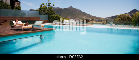 Frau Sonnenbaden auf Liegestuhl neben Luxus-Pool mit Blick auf die Berge Stockfoto