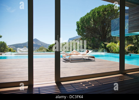 Frau Sonnenbaden auf Liegestuhl neben Luxus-Pool mit Blick auf die Berge Stockfoto