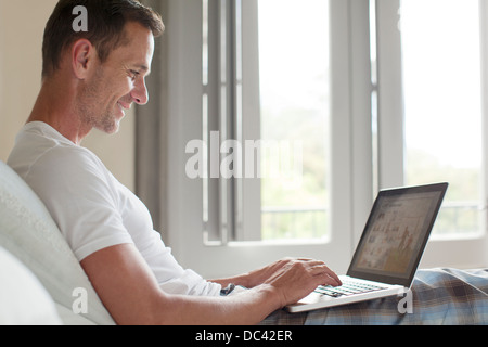 Lächelnder Mann mit Laptop im Bett Stockfoto