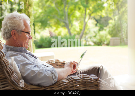 Senior woman mit digital-Tablette in Wicker Sessel auf Veranda Stockfoto