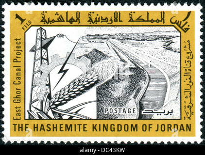 Jordanien - ca. 1963: Eine Briefmarke gedruckt in Jordanien, zeigt Osten Ghor Canal, Pylon, Zahnrad und Weizen ca. 1963 Stockfoto