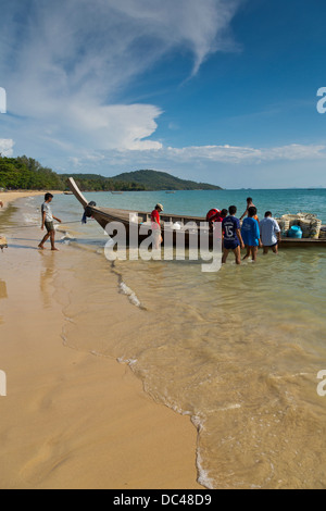 Thai Fischer Entladen einer traditionellen Longtail-Boot an einem einsamen Strand in Ao Nang, Thailand Stockfoto