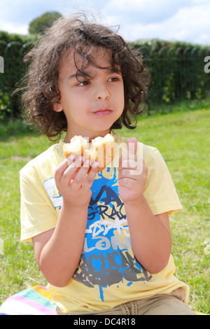 Kleiner Junge einen Donut im Park zu essen. Stockfoto