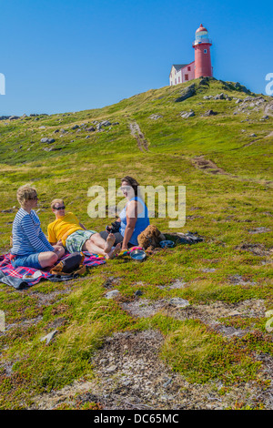 Kanadier, zwei Frauen und ein Mann in den Zwanzigern, Picknick draußen auf dem Boden unterhalb des Leuchtturms Ferryland in Neufundland. Stockfoto