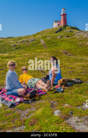 Kanadier, zwei Frauen und ein Mann in den Zwanzigern, Picknick draußen auf dem Boden unterhalb des Leuchtturms Ferryland in Neufundland. Stockfoto