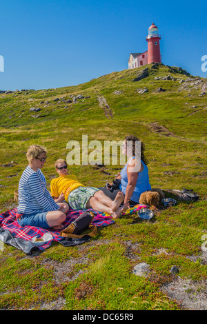 Kanadier, zwei Frauen und ein Mann in den Zwanzigern, Picknick draußen auf dem Boden unterhalb des Leuchtturms Ferryland in Neufundland. Stockfoto