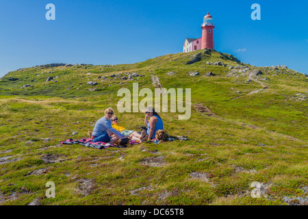 Kanadier, zwei Frauen und ein Mann in den Zwanzigern, Picknick draußen auf dem Boden unterhalb des Leuchtturms Ferryland in Neufundland. Stockfoto