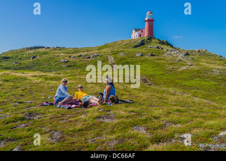 Kanadier, zwei Frauen und ein Mann in den Zwanzigern, Picknick draußen auf dem Boden unterhalb des Leuchtturms Ferryland in Neufundland. Stockfoto