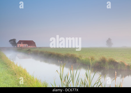 Bauernhaus am Ufer im Morgennebel bei Sonnenaufgang Stockfoto