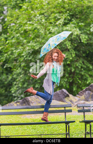 Frau mit Regenschirm tanzen auf der Bank im park Stockfoto