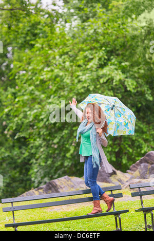 Frau mit Regenschirm tanzen auf der Bank im park Stockfoto