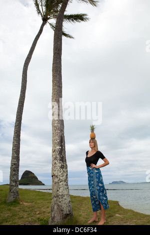 Eine blonde Frau Caucasion steht unter einer Palme mit Ananas auf dem Kopf. Stockfoto