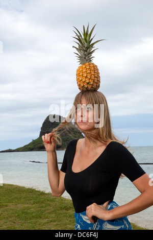 Eine blonde Frau Caucasion steht unter einer Palme mit Ananas auf dem Kopf. Stockfoto