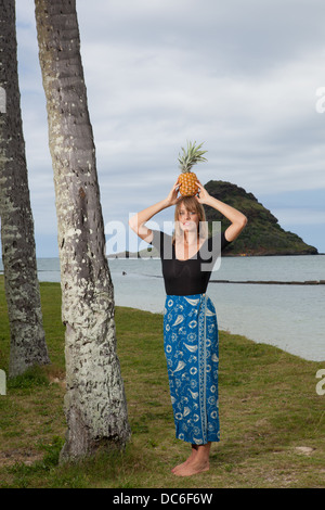 Eine blonde Frau Caucasion steht unter einer Palme mit Ananas auf dem Kopf. Stockfoto