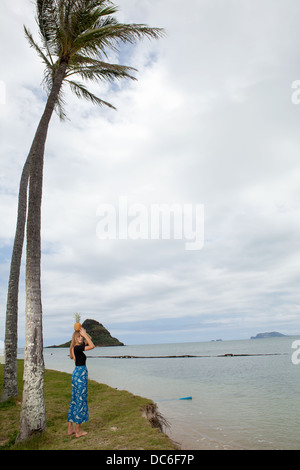 Eine blonde Frau Caucasion steht unter einer Palme mit Ananas auf dem Kopf. Stockfoto