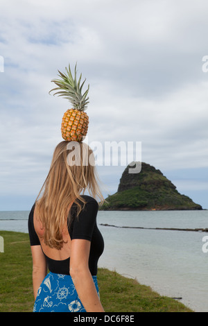 Eine blonde Frau Caucasion steht unter einer Palme mit Ananas auf dem Kopf. Stockfoto