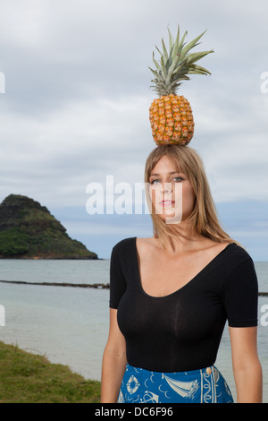 Eine blonde Frau Caucasion steht unter einer Palme mit Ananas auf dem Kopf. Stockfoto