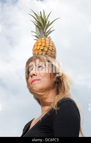 Eine blonde Frau Caucasion steht unter einer Palme mit Ananas auf dem Kopf. Stockfoto