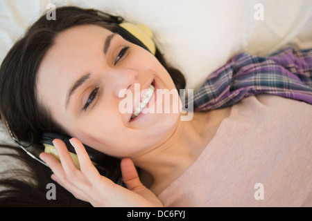 Porträt der jungen Frau auf dem Bett liegend und Musik hören Stockfoto