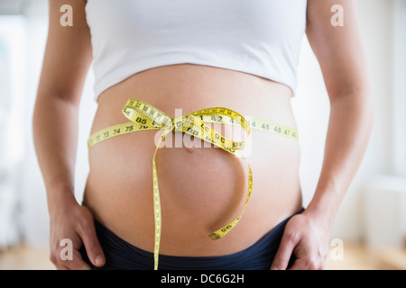 Mittelteil der schwangeren Frau mit Maßband gefesselt auf dem Bauch Stockfoto