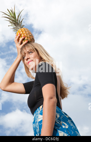 Eine blonde Kaukasische Frau steht eine Ananas auf dem Kopf halten. Stockfoto