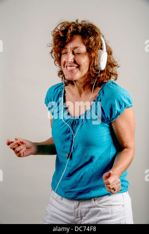 Eine 50 Jahre alte Auburn dunkelhaarige Frau genießt Musik über Kopfhörer. Stockfoto