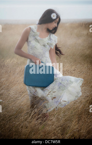 ein Mädchen in einem geblümten Kleid auf einem Feld mit einem Koffer Stockfoto