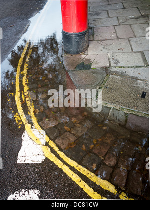 Große Pfütze im Rinnstein der Straße, mit roten Briefkasten Stockfoto