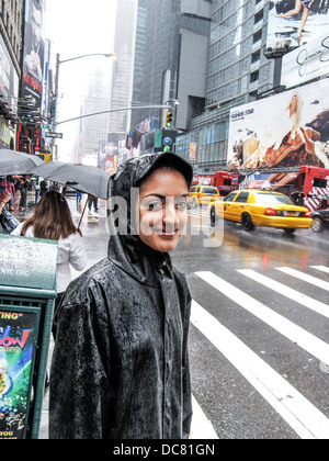 junges hübsches Mädchen tragen schwarze wasserdichte Jacke mit Kapuze steht im Zebrastreifen am Broadway in Times Square Gegend im strömenden Regen Stockfoto