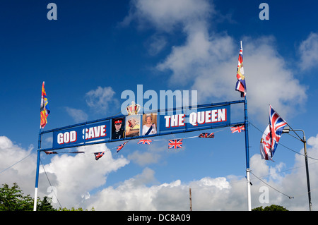 Eine Orange Bogen über eine Straße in Kilkeel mit Fahnen, Fotos von der Queen und Prinz William, mit "God Save The Queen" Stockfoto