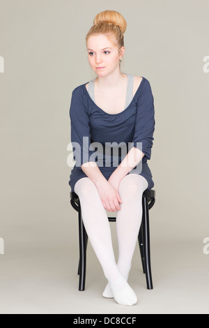 Nachdenkliche junge blonde weibliche Teenager im Ballett Kleid auf Stuhl sitzend Stockfoto