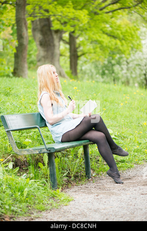 Eine junge attraktive Frau sitzen auf Bank in einem Park in ein Tagebuch zu schreiben
