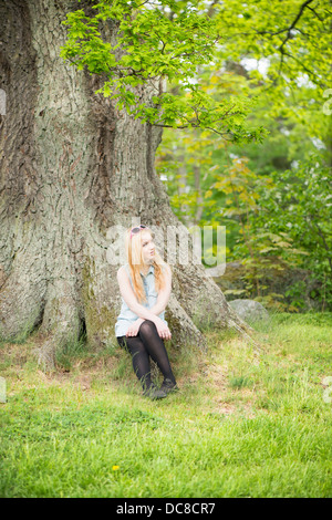 Natur-Szene mit einer jungen attraktiven Frau sitzt bei einem Baum in einem park Stockfoto