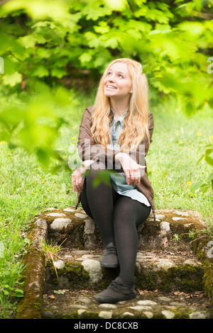 Natur-Szene mit einer jungen attraktiven blonden Frau sitzt in einem Park, Blick nach oben Stockfoto