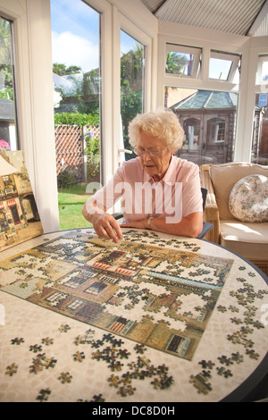 Zog sich Frau macht eine Puzzle in ihrem Wintergarten genießen einen bescheidenen Lebensstandard im England, United Kingdom Stockfoto