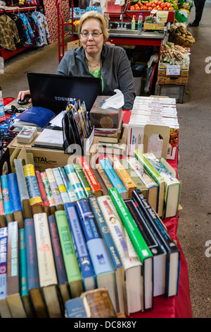 Ein Frau Buchhändler sitzt an ihrem Stand in der City Market und befasst sich mit ihrem Computer in St. John, Nova Scotia, Kanada. Stockfoto