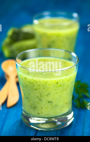 Zucchini Creme Suppe serviert in Gläsern auf blaue Holz mit Holzlöffel, Petersilie und kleine zucchini Stockfoto