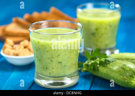 Zucchini Creme Suppe serviert in Gläsern auf blaue Holz mit kleinen Zucchini und Petersilie auf die Seite, Croutons und Toast Brot Stockfoto