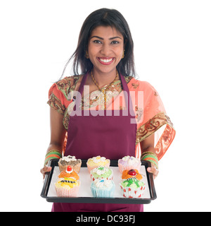 Traditionelle indische Frau in Sari backen Brot und Muffins, trägt Schürze halten Behälter isoliert auf weiss. Stockfoto